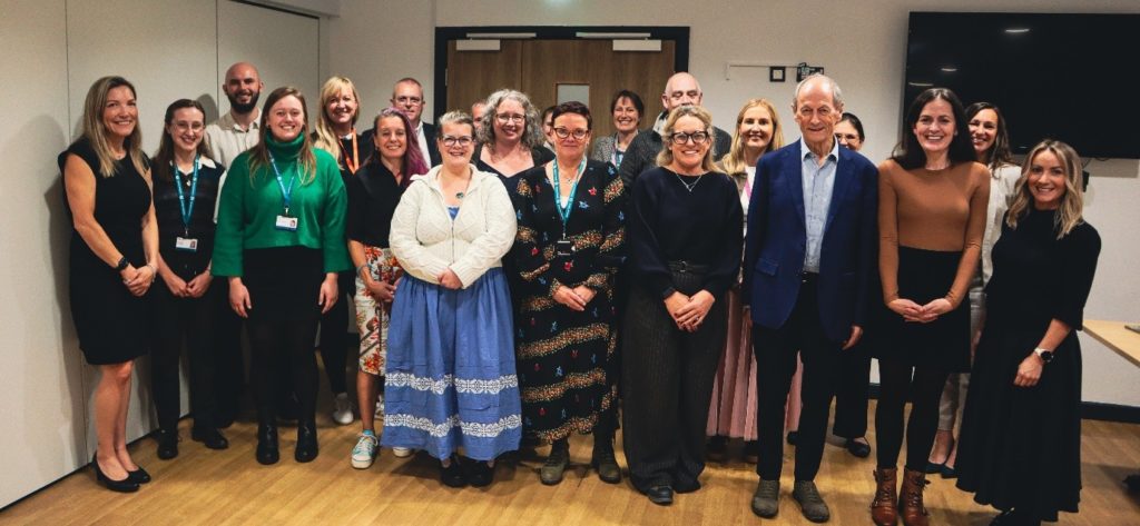 A group of twenty people pose together indoors, standing in rows and smiling at the camera.