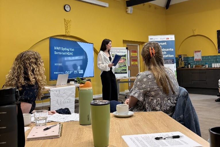 Presenter speaking to attendees during a workshop, with a presentation displayed on a screen.